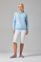 Buy Online Petula Pullover Alice Collins -  Woman wearing a light blue sweater with star patterns and white pants on a gray background