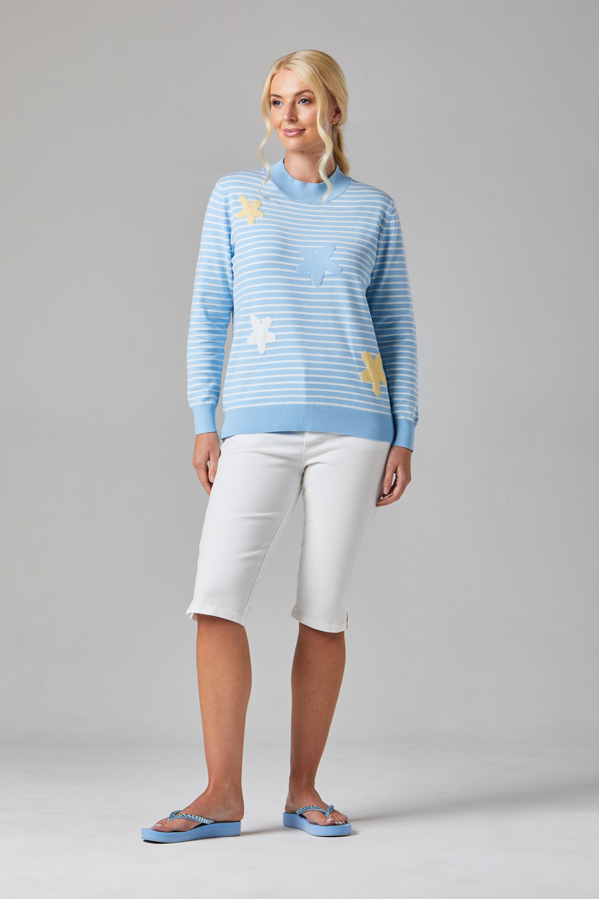 Buy Online Petula Pullover Alice Collins -  Woman wearing a light blue sweater with star patterns and white pants on a gray background