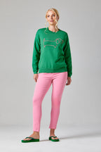 Buy Online Sausage Dog Pullover Alice Collins - Woman wearing a green sweater with a fish design and pink pants on a gray background