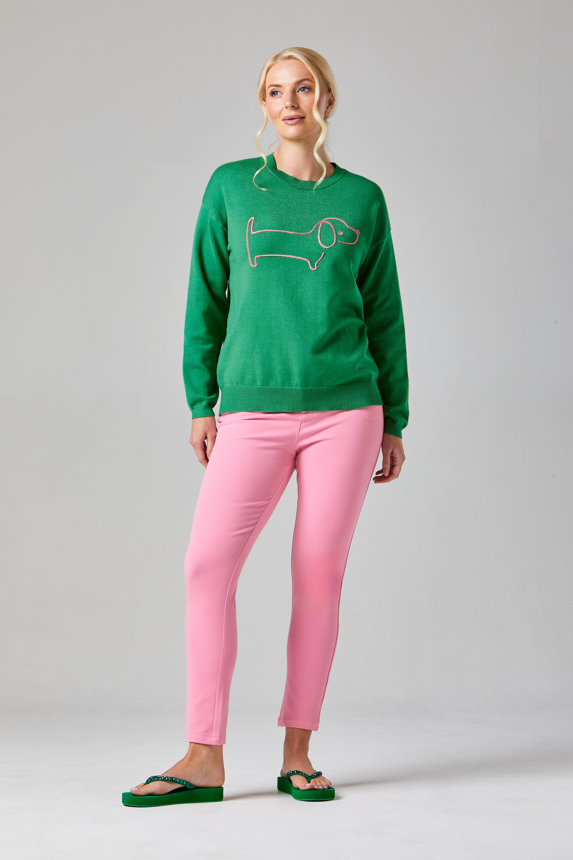 Buy Online Sausage Dog Pullover Alice Collins - Woman wearing a green sweater with a fish design and pink pants on a gray background
