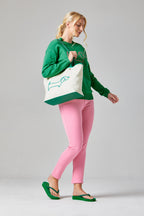 Buy Online Sausage Dog Pullover Alice Collins -Woman holding a tote bag with a green design, wearing a green sweatshirt and pink pants on a gray background