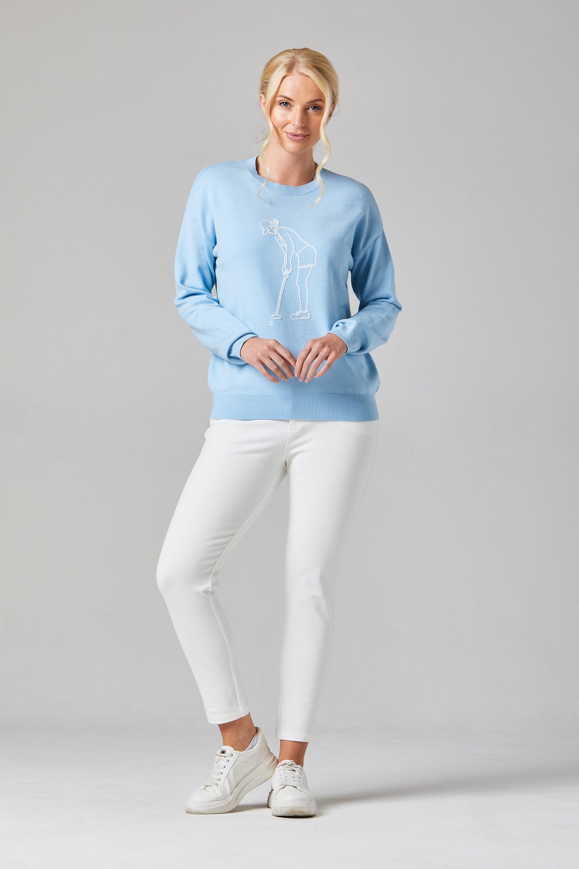 Buy Online Lady Golfer Pullover Alice Collins Woman wearing a light blue sweater with a design and white pants on a gray background