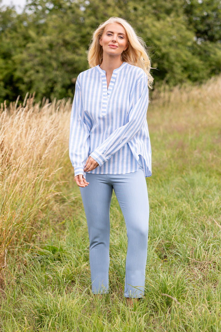 Megan Shirt Buy Online Alice Collins Woman wearing a light blue striped shirt and jeans standing in a grassy field.